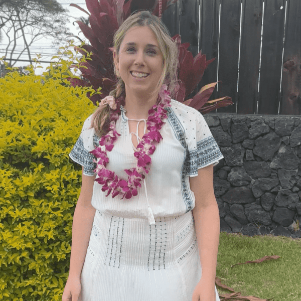 Smiling woman in white dress with flower lei outdoors.