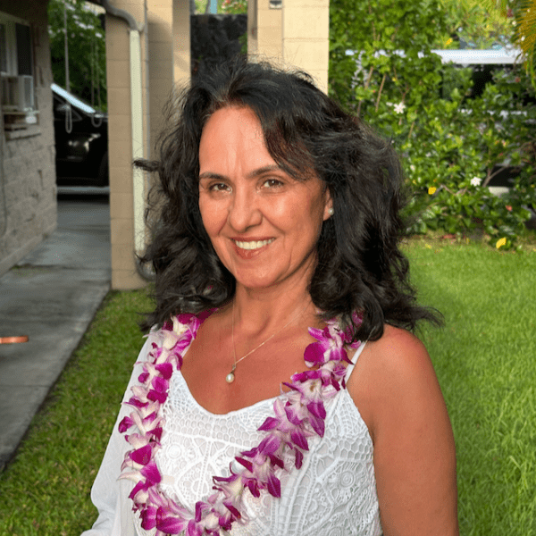 A smiling woman wearing a purple lei and white top outdoors.