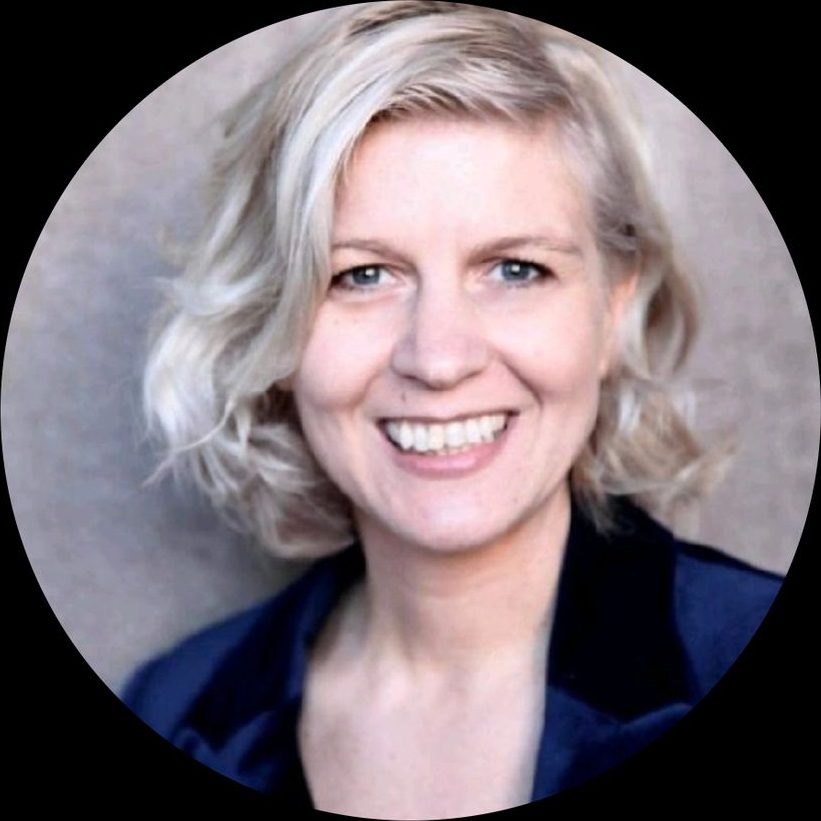 Smiling woman with short blonde hair wearing a dark blazer.