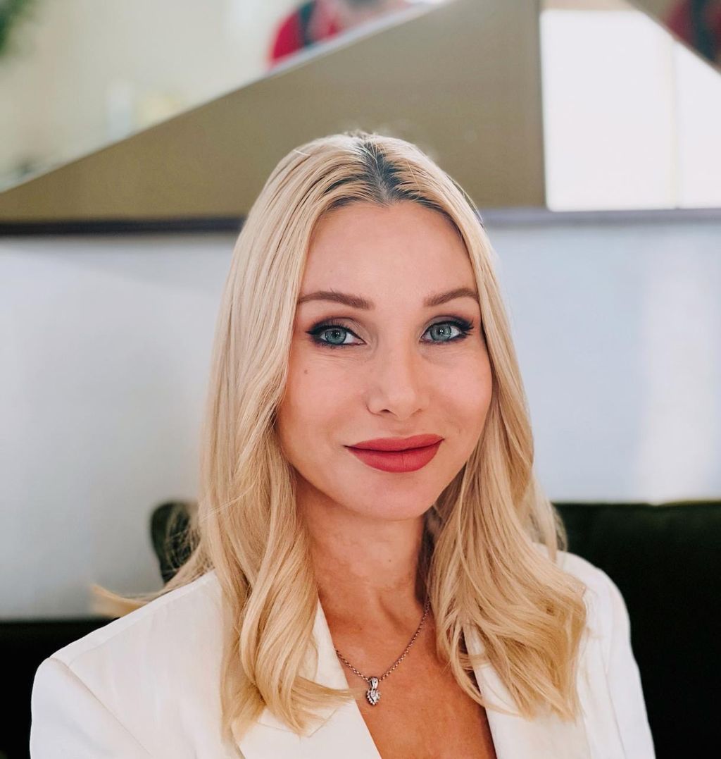 Professional blonde woman smiling in a modern indoor setting.